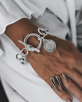 Silver Phaistos Disc Bracelet features an asymmetric link chain, large toggle closure, and a detailed teardrop pendant.