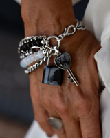 Five-strand bracelet featuring moonstone beads and black glass, with a lock and key charm, worn on a wrist.
