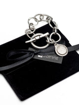 Silver Phaistos Disc bracelet with large toggle clasp, asymmetrical metal links, and a teardrop-shaped pendant.