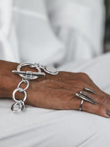 Silver Phaistos Disc bracelet features an asymmetrical link chain and large toggle closure, adorned with a teardrop pendant.