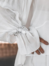 Silver Phaistos Disc Bracelet featuring an asymmetric link chain, large toggle closure, and teardrop pendant, worn on a draped white blouse.