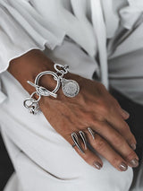 Silver Phaistos Disc Bracelet with asymmetric link chain, large toggle closure, and teardrop pendant displayed on a hand.