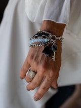 Multi-strand bracelet featuring moonstone, black glass beads, and a lock and key charm, worn on a model's wrist.