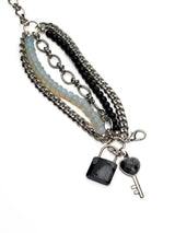 Five-strand bracelet featuring layering of luminous moonstone, black glass beads, and a lock and key pendant.