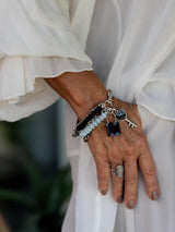 Hand wearing a five-strand Moonstone bracelet with black glass beads and a lock and key charm, styled in an edgy boho look.