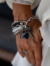 Five-strand bracelet featuring luminous moonstones, black glass beads, and a lock and key charm, styled on a wrist.