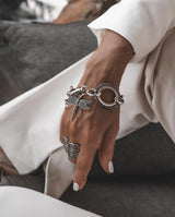 Chunky silver bracelet with a detailed dragonfly pendant, worn on a model’s wrist, complemented by a silver ring.