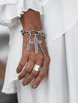 Stainless steel cross hand chain bracelet featuring a large gothic cross pendant, worn elegantly with a silver ring.