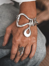 Chunky silver toggle cuff bracelet worn on a wrist, featuring a hefty design, T-bar clasp, and large drop pendant.