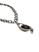 A close-up of a silver-toned chain necklace with a stylized eye pendant featuring a glossy black center, set against a plain white background.
