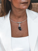A close-up of a woman wearing a silver-toned chain necklace with a faceted black pendant, styled with a white blazer.