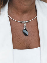 A close-up of a person wearing a silver-toned choker necklace with a faceted black gemstone pendant, styled with a white top and white blazer.