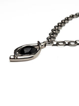 A close-up of a silver-toned chain necklace with a unique teardrop-shaped pendant featuring a smooth, polished black center, set against a plain white background.