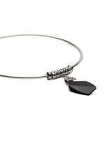 A silver wire bangle bracelet featuring a textured cylindrical bead and a dangling black shield-shaped charm, shown on a plain white background.