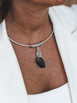 A close-up of a person wearing a silver-toned choker necklace with a faceted black pendant, styled with a white blazer.