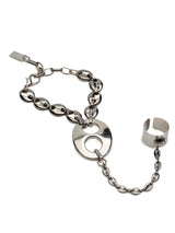 A silver-toned metal bracelet featuring a central circular disc charm connected by a chain to a matching open cuff, photographed on a plain white background.