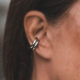 Asymmetric metal ear cuffs displayed on the outer cartilage of an ear, featuring a bold and minimal design.