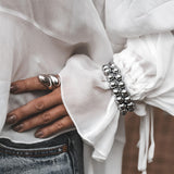 Hematite beaded wrap bracelet featuring 12mm dark gray beads and silver accents, worn on a wrist with a flowing white blouse.