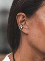 Asymmetric metal ear cuffs worn on the ear, showcasing a bold, mismatched design with one larger and one smaller cuff.
