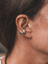 Asymmetric metal ear cuff worn on the upper cartilage of an ear, featuring a bold, shiny design with a minimalist style.