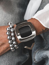 Chunky hematite beaded wrap bracelet with silver accents, styled with a large metallic buckle cuff, worn on a denim-clad wrist.
