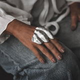 Chunky silver knuckle ring with a sculptural, irregular pleated design, showcased on a hand resting on denim.