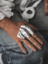 Chunky melted zinc alloy ring with an irregular, folded texture, styled on a hand resting on denim.