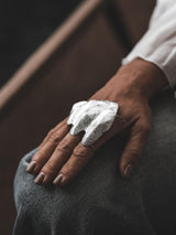 Chunky, sculptural knuckle ring in irregular, textured zinc alloy, worn on a hand resting on denim.