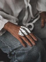 Sculptural folded metal ring in silver, featuring an irregular, textured design worn on a model's hand.